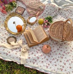 an open book sitting on top of a blanket next to two mirrors and some fruit