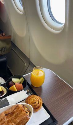 an airplane meal with orange juice and fruit on the tray next to it is sitting in front of a window