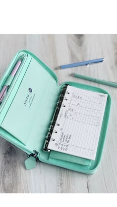 a green folder with two pens and a notepad in it sitting on a table