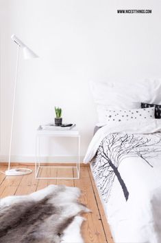 a bedroom with white walls and wood flooring has a black and white tree print on the bed