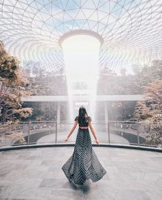 a woman standing in front of a fountain with her arms spread out and looking at the ground