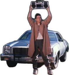 a man holding up a radio above his head in front of a car