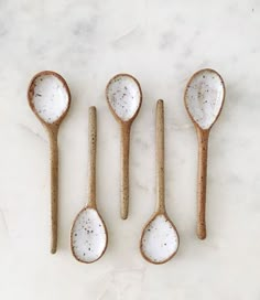 five spoons are lined up in the shape of small spoons with speckled white paint on them