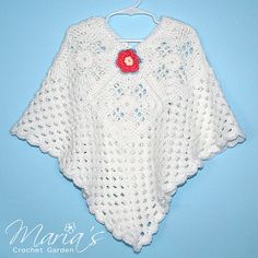 a white crocheted ponchle with a red flower on it