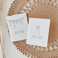 two cards with the words hello baby on them are sitting on a doily next to a straw hat