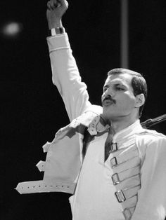 a man in white shirt and tie standing on stage with his hand up to the sky