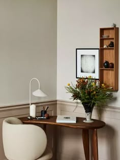 a room with a table, chair and vase on the floor in front of it