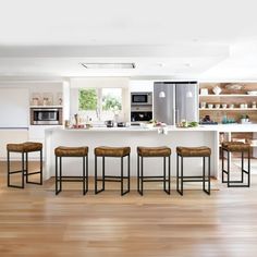 a kitchen with white walls and wooden floors has stools in front of the bar