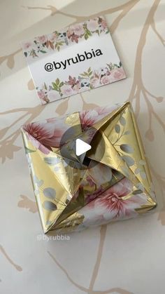 an origami envelope with gold foil and pink flowers is on display in front of a floral wallpaper