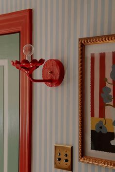 a red light switch sitting on the side of a wall next to a striped wallpaper