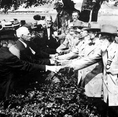 an old black and white photo of men in suits shaking hands with each other outside