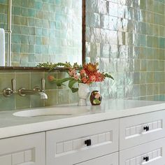 a bathroom with green tiles on the wall and white cabinets, along with a vase filled with flowers