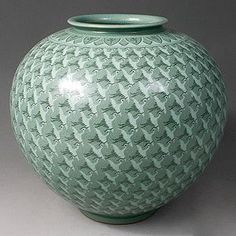 a large green vase sitting on top of a white table next to a gray wall