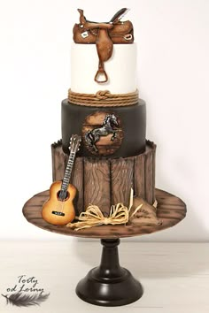 a three tiered cake with a guitar and cowboy theme on the top, sitting on a wooden stand