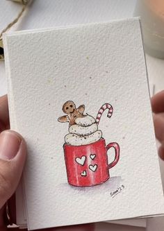 a hand holding up a card with a drawing of a cup of coffee and a candy cane