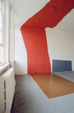 an empty room with red and white paint on the wall, next to a radiator