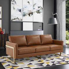 a brown leather couch sitting on top of a rug in front of a wall mounted painting