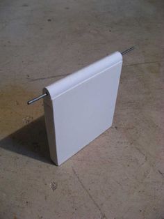 a small white object sitting on top of a cement floor next to a metal pole