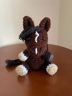 a crocheted brown and white horse sitting on top of a wooden table