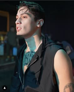 a young man with tattoos on his arm and chest standing in front of a crowd