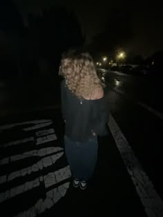 a woman standing on the side of a road at night with her back turned to the camera