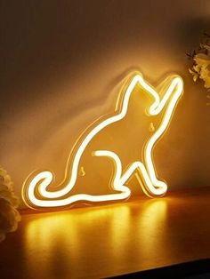 a cat shaped neon sign sitting on top of a wooden table next to a vase with flowers