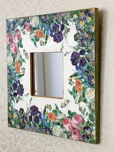 a mirror mounted to the side of a wall with flowers on it and a wooden frame