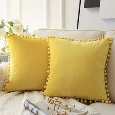 two yellow pillows sitting on top of a white couch next to a vase with flowers