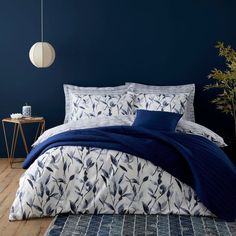 a bed with blue sheets and pillows in a room next to a plant on the floor