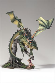 a statue of a green dragon with two people standing next to it on a white surface