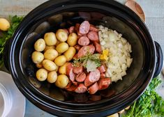 a crock pot filled with potatoes, meat and onions next to other vegetables on a table