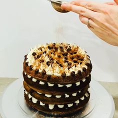 a person is sprinkling icing on a chocolate cake with white frosting