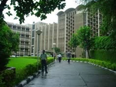 people are walking down the sidewalk in front of tall buildings with green trees on either side