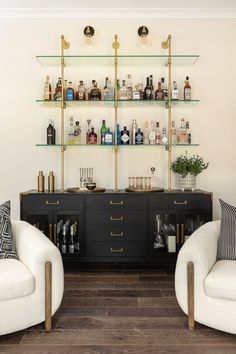 two white chairs sitting next to each other in front of a shelf filled with bottles