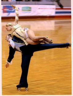 two people on roller skates in an indoor arena, one holding the other's leg