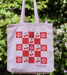 Pack up a picnic in this vibrant pink tote bag, displaying a checkerboard of cherries and cherry blossoms. It's the perfect accessory for spring! Spring Picnic Cotton Bag, Retro Pink Cotton Bag, Retro Cotton Bags For Spring, Summer Cotton Bag For Picnic, Cotton Summer Picnic Bag, Cotton Picnic Bag For Summer, White Cotton Picnic Bags, White Cotton Picnic Bag, Red Spring Picnic Bag