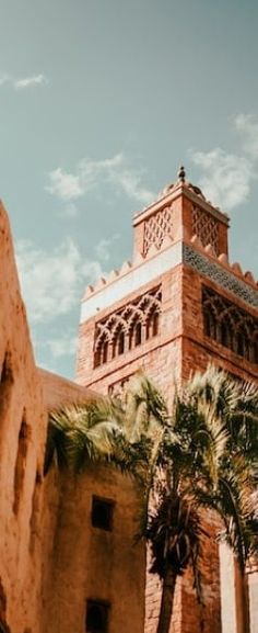 a tall brick building with a clock on it's side and palm trees in the foreground