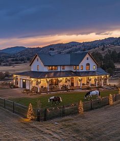 two horses are grazing in front of a large house with christmas lights on the fence