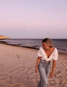 a woman walking across a sandy beach next to the ocean