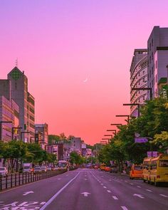 an empty street with cars parked on both sides and buildings in the background at sunset