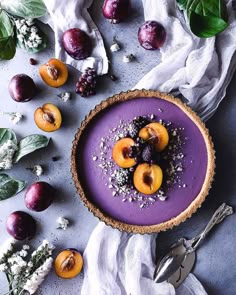 a dessert with plums and other fruits on a gray surface next to silverware