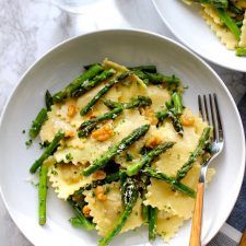 two white plates filled with pasta and asparagus on top of a marble table