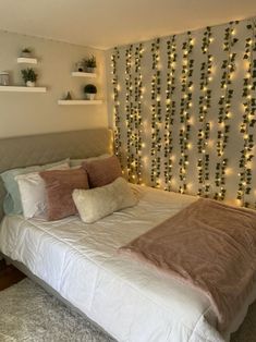 a white bed topped with lots of pillows next to a wall covered in christmas lights