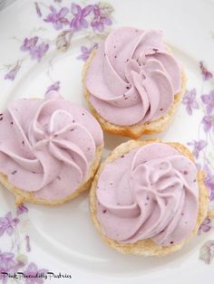 three cupcakes with pink frosting on a white and purple flowered plate