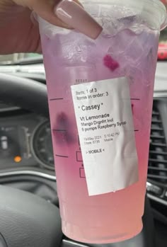 a person holding up a drink in their hand with pink liquid and ice on it