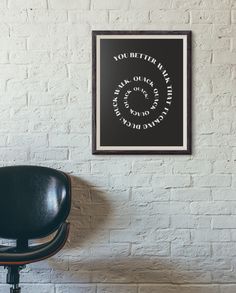 a black chair in front of a white brick wall with a framed poster on it