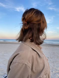 a woman standing on top of a sandy beach next to the ocean with her hair in a bun