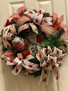 a christmas wreath with red and white bows hanging on the front door, decorated with ornaments