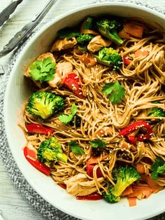 a white bowl filled with noodles, broccoli and other vegtables