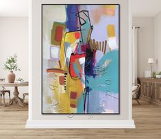 an abstract painting hangs on the wall above a table in a room with wooden floors